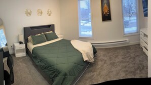 A bedroom with a bed, nightstands, a dresser, and a large window with blinds.