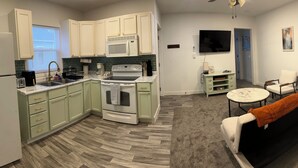 A compact kitchen with white cabinets, a microwave, and a stove. There is a dining area with a black sofa and a small round table.