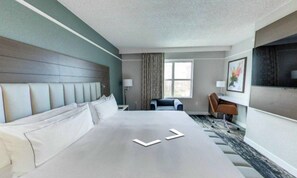 Habitación de hotel con una cama grande, un escritorio, una silla y una ventana con cortinas.