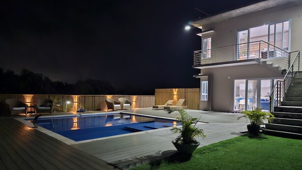 Une maison moderne dotée d’une piscine, d’un espace salon extérieur et d’un balcon bien éclairé.