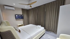Une chambre d’hôtel moderne équipée d’un lit, d’un téléviseur fixé au mur, d’un ventilateur de plafond et d’une grande fenêtre avec des rideaux.