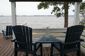 Un espacio de estar al aire libre cubierto con dos sillas Adirondack y una mesa, con vista a un cuerpo de agua.