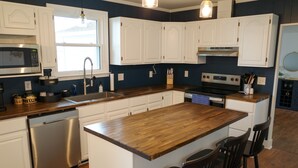 A modern kitchen with white cabinets, a wooden island, and a stainless steel dishwasher. - Riverfront Retreat on Perquimans: Cozy Fire Pit, Golf Minutes Away, Serene Views (Hertford)