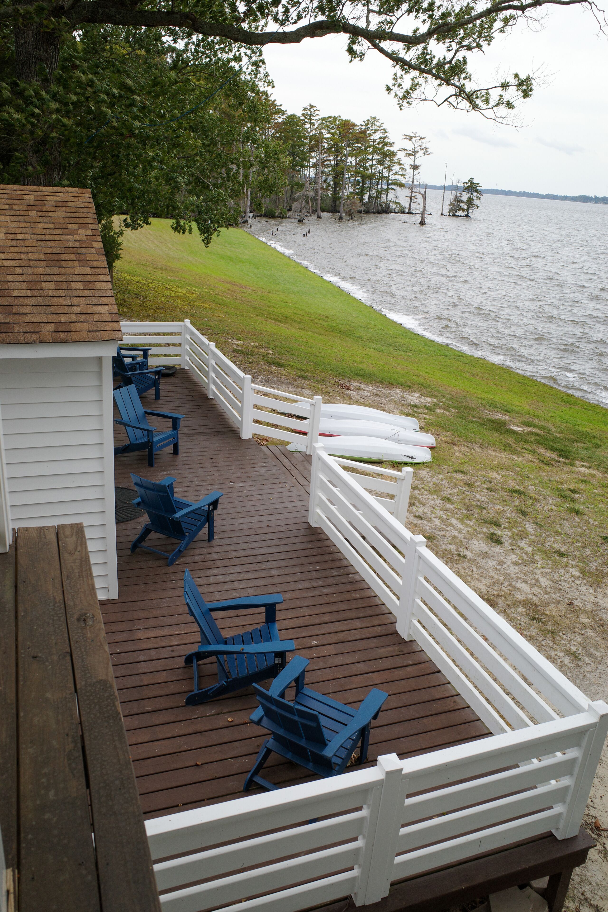 A wooden deck with blue chairs and a white railing overlooking a body of water.