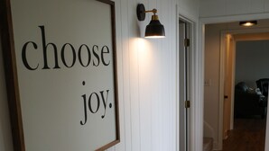A hallway with wooden flooring and a framed sign that reads "choose joy." - Riverfront Retreat on Perquimans: Cozy Fire Pit, Golf Minutes Away, Serene Views (Hertford)