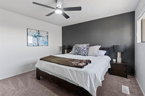 A bedroom with a bed, two bedside tables, a ceiling fan, and a wall-mounted abstract painting.