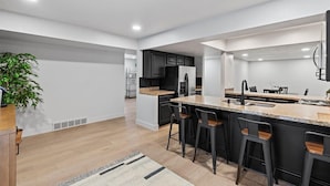 A modern kitchen with a central island, black bar stools, and a potted plant. - The House Between 2 Canyons (Cottonwood Heights)