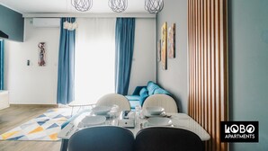 Una sala de estar moderna con comedor, que incluye un sofá, una mesa de comedor con platos y vasos, y una alfombra estampada.