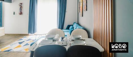 Una sala de estar moderna con comedor, que incluye un sofá, una mesa de comedor con platos y vasos, y una alfombra estampada.