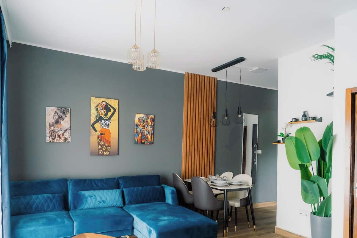 Ein modernes Wohnzimmer mit einem blauen Modulsessel, einem Esstisch und einer großen Grünpflanze.
