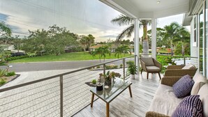 A balcony with a view of a green landscape, a glass table with plants, wicker furniture, and a metal railing. - Tropical Siesta Key Getaway | Heated Private Pool + Fire Pit | 4BR Sleeps 10 | Minutes to Siesta Beach & Village! (Siesta Key)