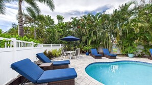 A poolside area with lounge chairs, a table, and an umbrella. - Tropical Siesta Key Getaway | Heated Private Pool + Fire Pit | 4BR Sleeps 10 | Minutes to Siesta Beach & Village! (Siesta Key)