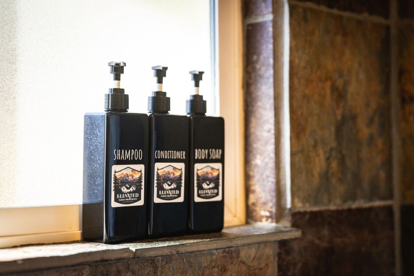Três garrafas de shampoo, condicionador e sabonete líquido em um peitoril.