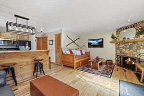 Un salon chaleureux avec une cheminée en pierre, des meubles en bois et une cuisine équipée d’appareils électroménagers modernes.
