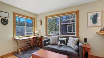 Ein gemütliches Wohnzimmer mit Ledersofa, Holztisch und Fenster mit Blick auf Bäume und Berge.