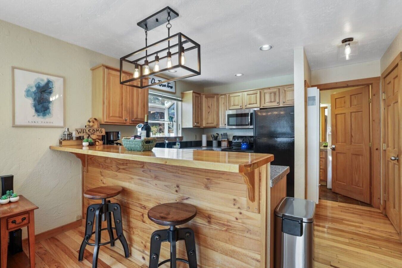 A kitchen with wooden cabinets, a bar area with stools, a hanging light fixture, and a stainless steel refrigerator.