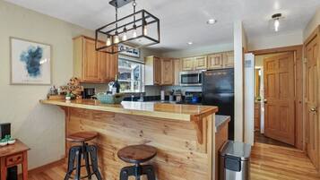 A kitchen with wooden cabinets, a bar area with stools, a hanging light fixture, and a stainless steel refrigerator.