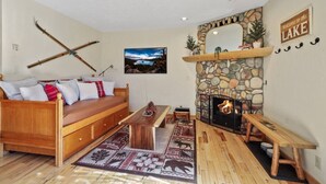 Ein gemütliches Wohnzimmer mit Kamin aus Stein, einer Holzcouch und Ski, die an der Wand lehnen.