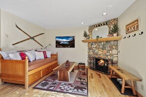 Un salon chaleureux avec une cheminée en pierre, un canapé en bois et des paires de skis appuyés contre le mur.