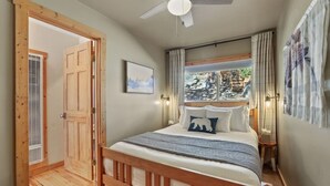 Ein Schlafzimmer mit einem Holzbett, einem Deckenventilator, einem Fenster mit Vorhängen und einer Tür zu einem anderen Raum.