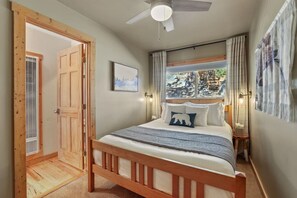 Une chambre avec un lit en bois, un ventilateur de plafond, une fenêtre avec des rideaux et une porte donnant sur une autre pièce.