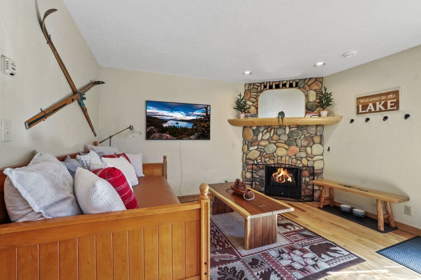 A cozy living room with a stone fireplace, a wooden bench, and a couch with pillows.