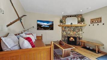 A cozy living room with a stone fireplace, a wooden bench, and a couch with pillows.