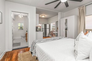 Una camera da letto con un letto, una ventola a soffitto, un bagno con il water e un lavandino, e una piccola cucina attrezzata con un frigorifero.