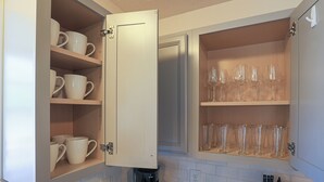 Een keuken met open kastjes, gevuld met mokken en wijnglazen.
