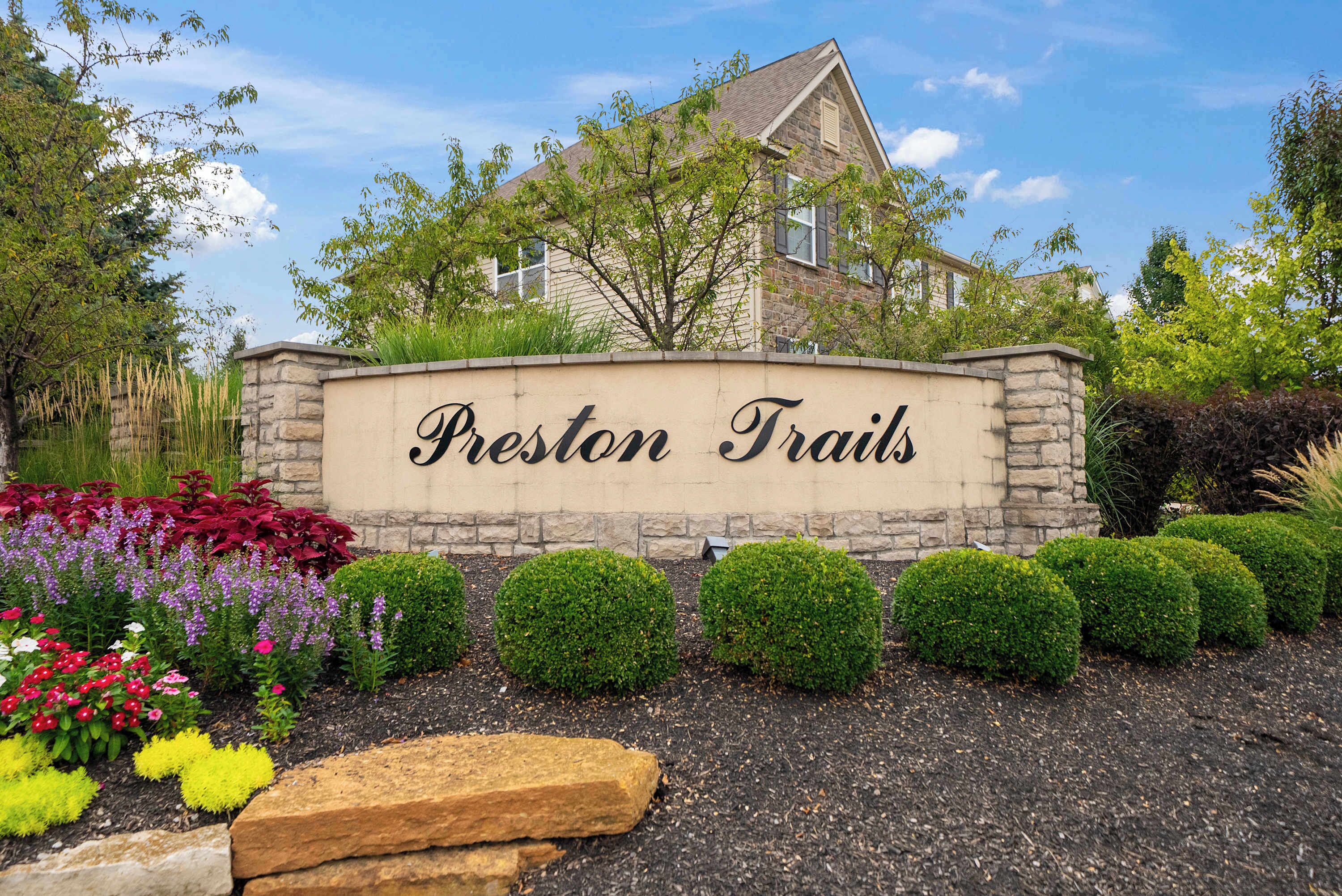 Un letrero de piedra con la inscripción 'Preston Trails', rodeado de jardines cuidados y arbustos podados.