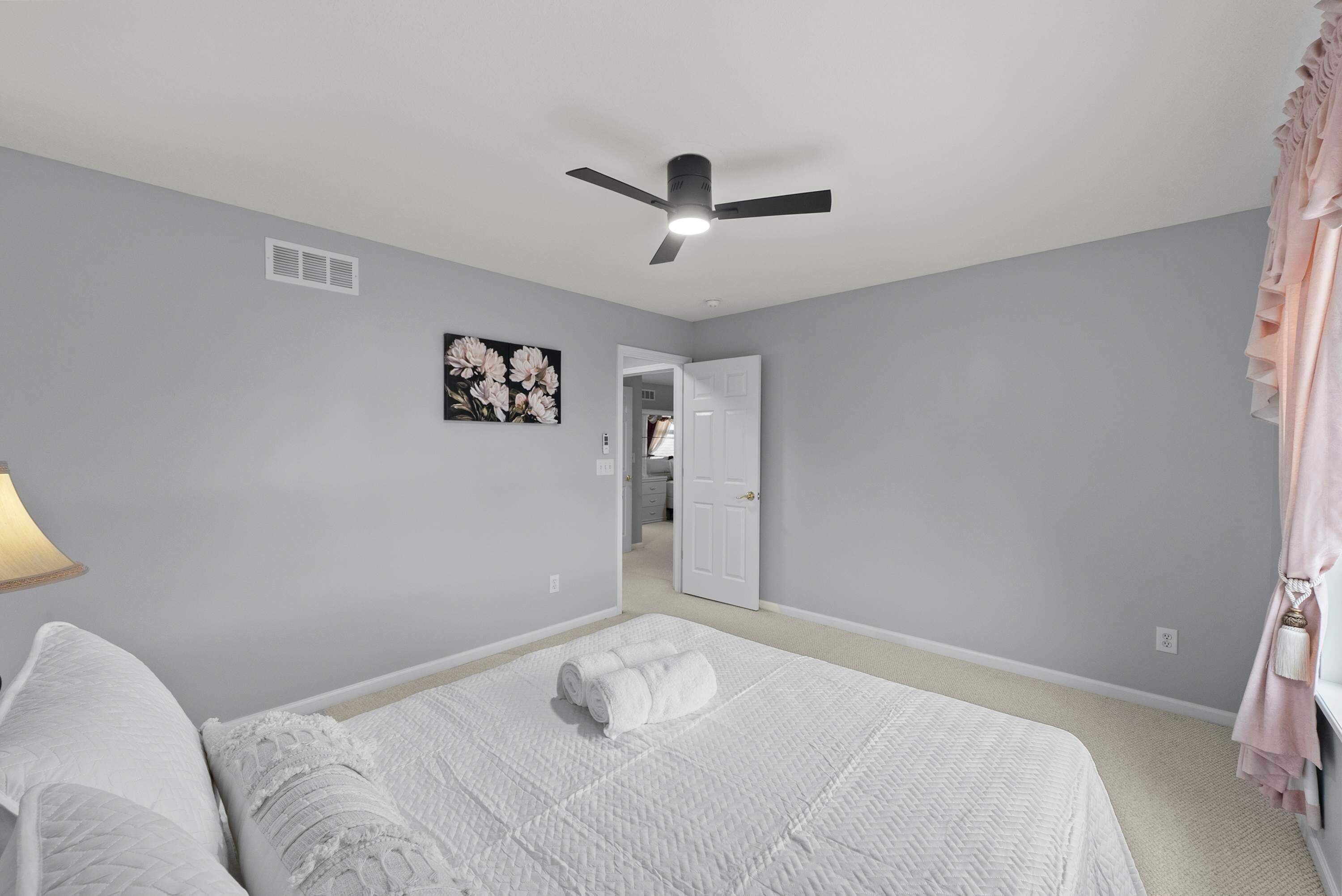 Ein Schlafzimmer mit einem Bett, einem Deckenventilator, einem Wandlüfter und einer Tür zu einem anderen Raum.