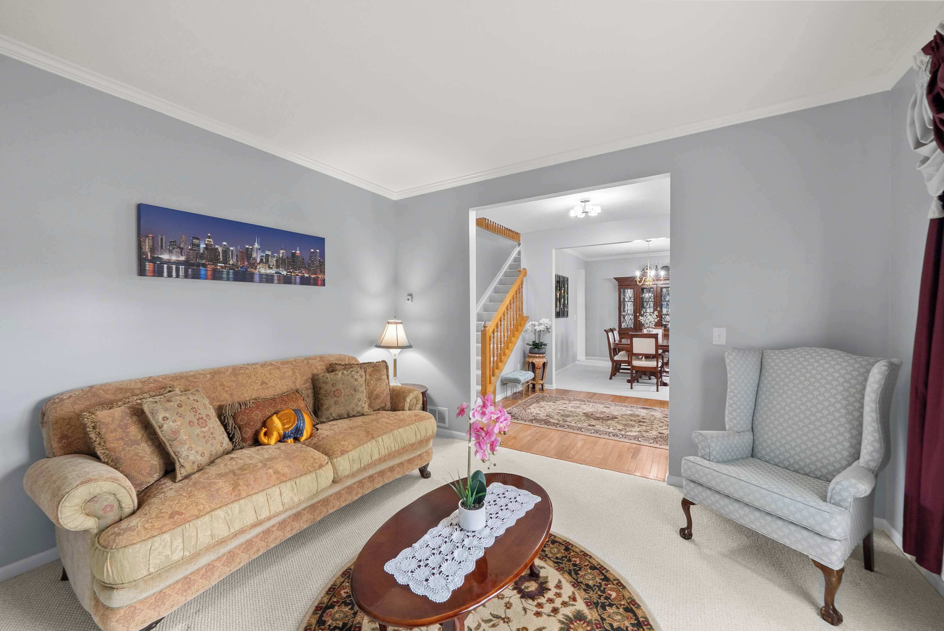 A living room with a sofa, armchair, coffee table, and a cityscape painting on the wall.