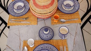 Una mesa para comer dispuesta con platos blancos y azules estampados, cubiertos y un protector de mesa tejido.