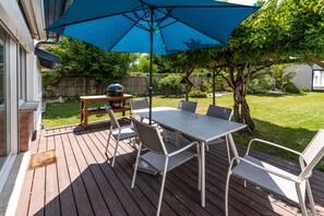 An outdoor patio with a table and chairs, a barbecue grill, and a blue umbrella.