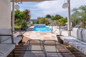 A covered outdoor area with a swimming pool, lounge chairs, and a pergola with hanging lights.