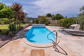 A rectangular swimming pool with a metal ladder, surrounded by a stone patio.