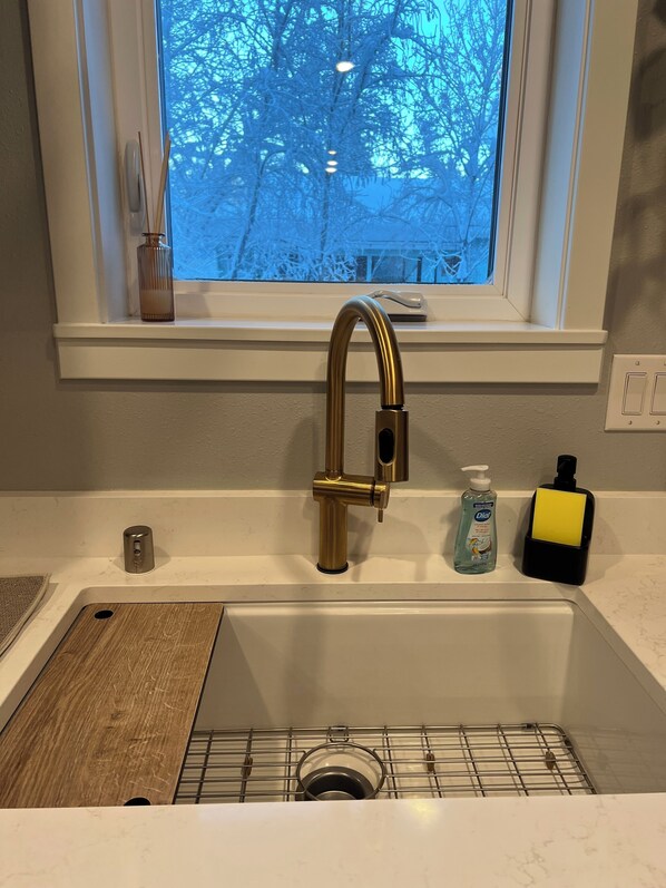 A kitchen sink with a gold faucet, a soap dispenser, and a dish soap bottle.