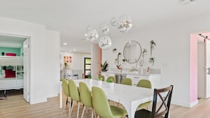 A modern kitchen with white cabinets, a white countertop, and a dining area with a white table and green chairs. - Disco Dino: Pool, HotTub & Game Room Sleeps 18 (Scottsdale)