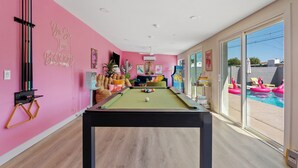 A pool table in a room with pink walls and a large window. - Disco Dino: Pool, HotTub & Game Room Sleeps 18 (Scottsdale)
