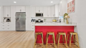 A modern kitchen with white cabinets, a stainless steel refrigerator, a microwave, and a red island with stools. - Disco Dino: Pool, HotTub & Game Room Sleeps 18 (Scottsdale)