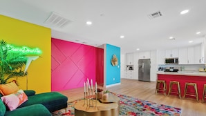 A modern living room with a vibrant color scheme, a kitchen area, and a neon sign. - Disco Dino: Pool, HotTub & Game Room Sleeps 18 (Scottsdale)