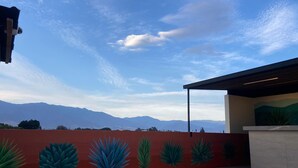A rooftop terrace with a red wall featuring large green plant designs, a tiled floor, and a view of distant mountains under a clear sky. - Casa Puro Verbo Candiani (Oaxaca)