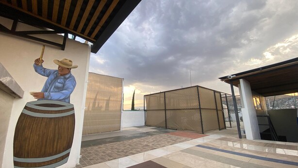 A rooftop terrace with a mural of a man playing a barrel organ, a fenced area, and a view of the sky. - Casa Puro Verbo Candiani (Oaxaca)