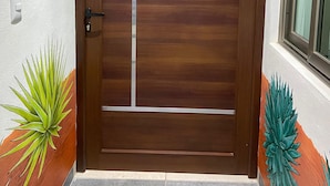 A wooden door with a metal handle and a glass panel, flanked by two decorative plants. - Casa Puro Verbo Candiani (Oaxaca)
