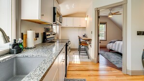 A compact kitchen with granite countertops, white cabinets, and a microwave. A dining area with a wooden table and chairs is visible through an open doorway. - Charming Apt w/ Shared Outdoor Space in Lisbon! (Lisbon)