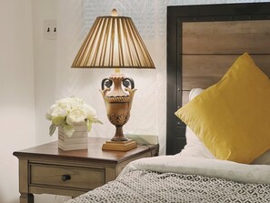 A bedroom with a wooden nightstand, a lamp, a bed with a patterned bedspread, and a yellow pillow. - Ramblei near Rittenhouse Sq | 1 bedroom – Unit A (Philadelphia)