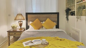 A bedroom with a bed, a bedside table with a lamp, a book, and a yellow throw blanket. - Ramblei near Rittenhouse Sq / 1 bedroom – Unit A (Philadelphia)