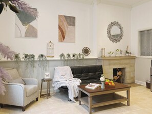 A living room with a sofa, a coffee table with a book and fruit, a fireplace, and wall art.