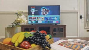 A living room with a flat-screen TV displaying a streaming service interface, a fruit bowl on the table, and a book. - Ramblei near Rittenhouse Sq / 1 bedroom – Unit A (Philadelphia)