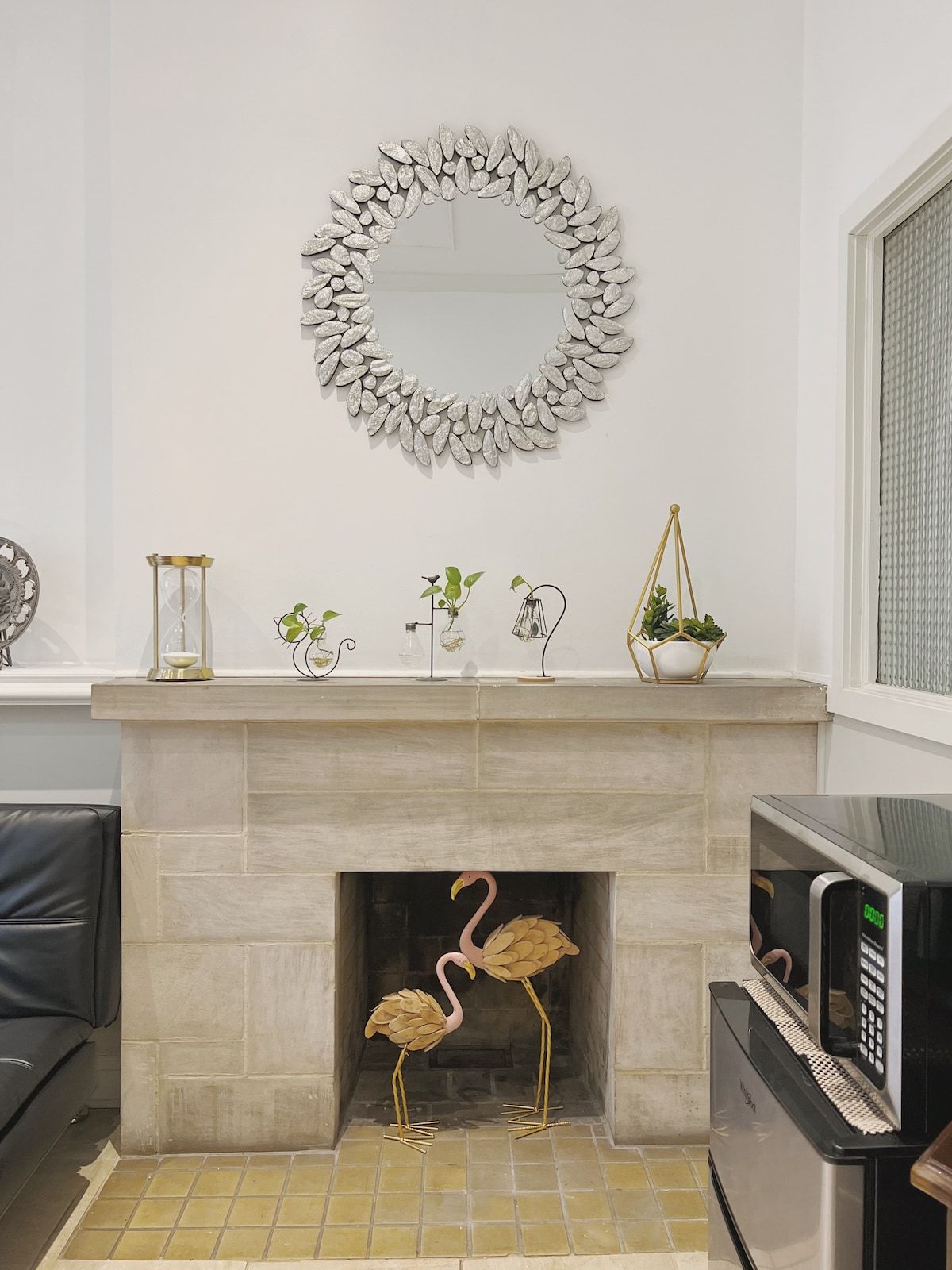 A fireplace with a decorative mirror above it, a small plant on the mantel, and a microwave to the right.
